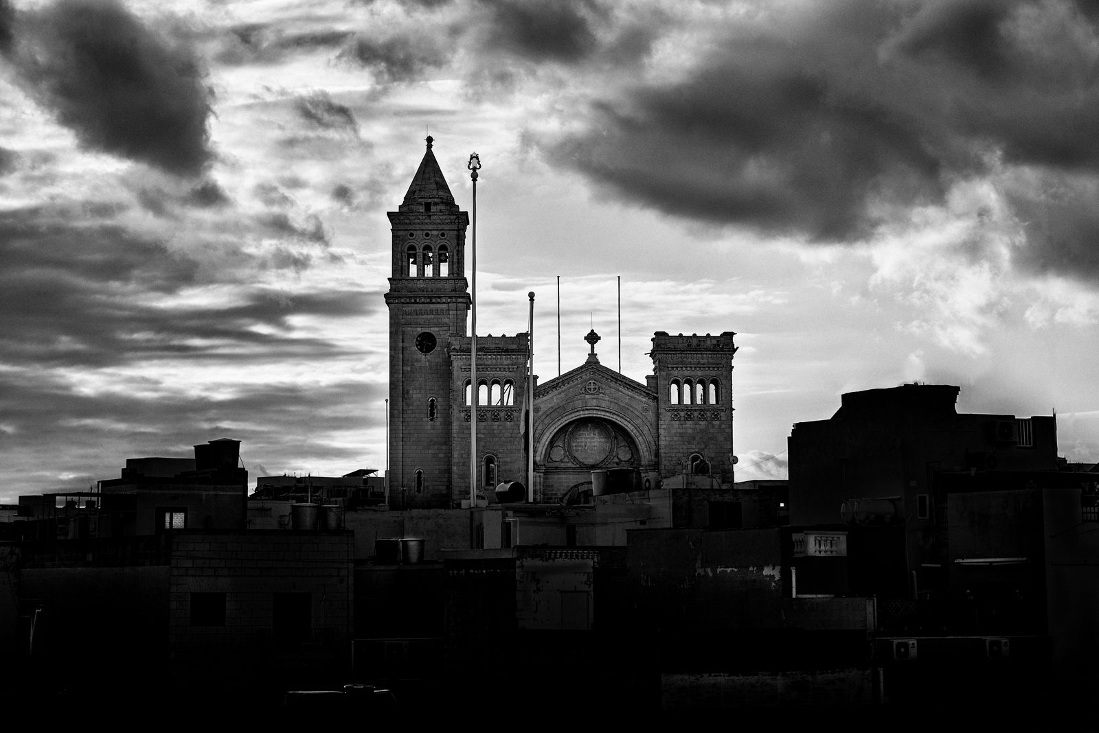 The parish church of San Pietru fil-Ktajjen above the rooftops of Birżebbuġa at sunset, black and white