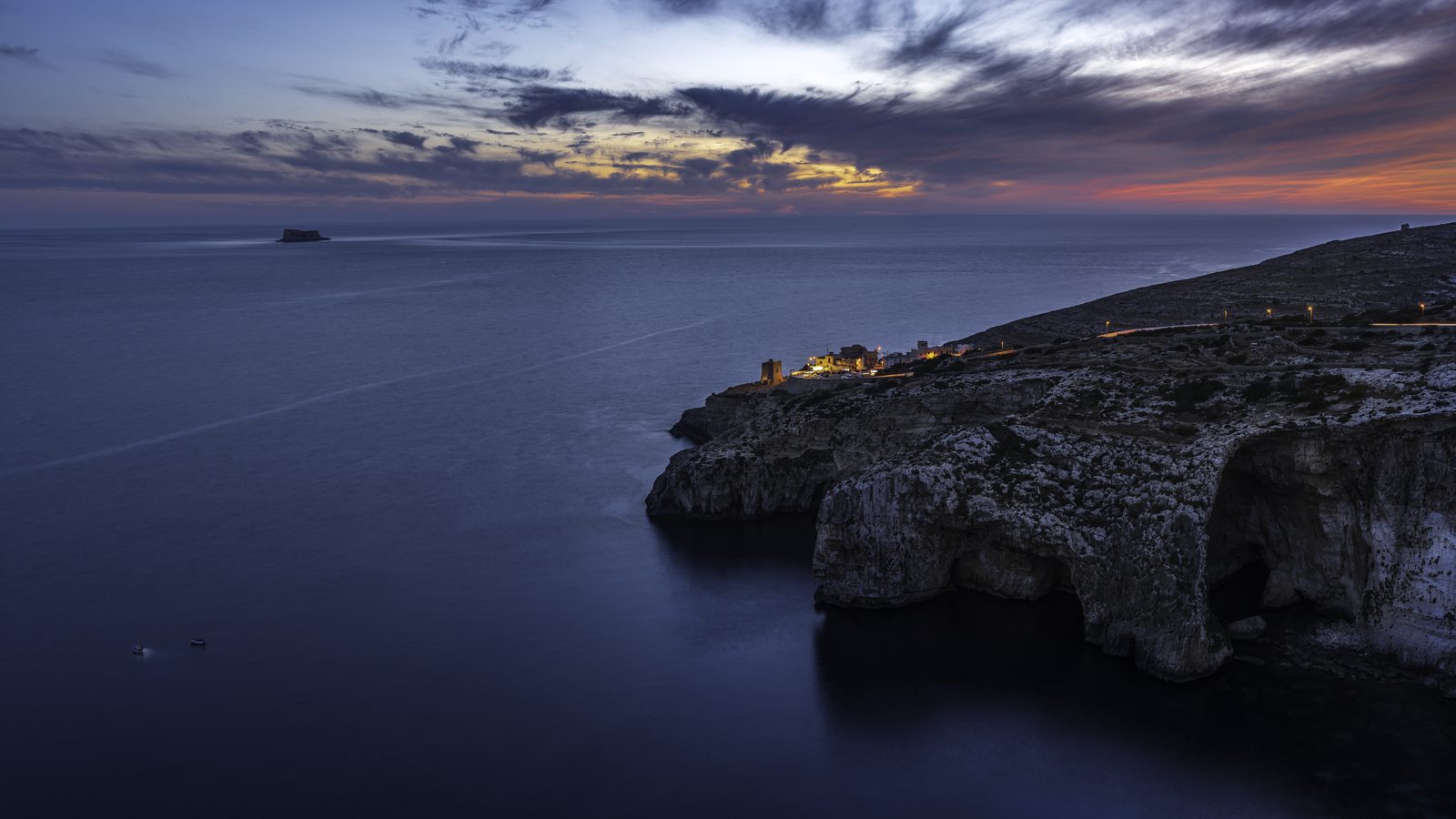 The Blue Grotto cliffs at blue hour with village lights and a long-exposure sea, Malta