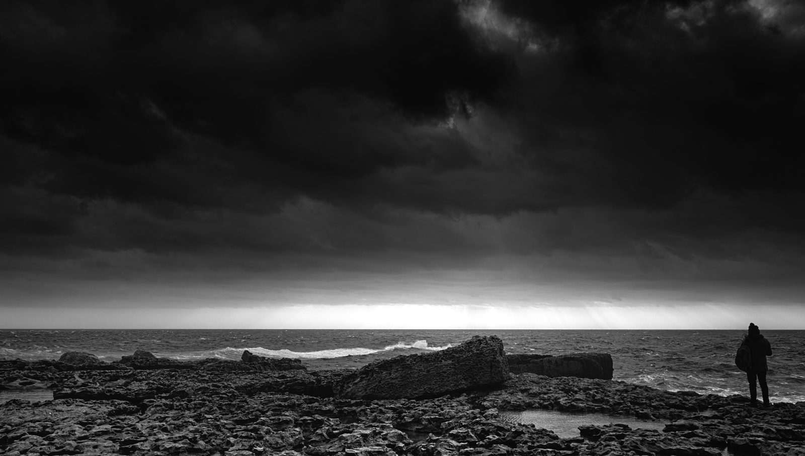 A girl facing a rough storm sea at Dwejra, Gozo, in black and white