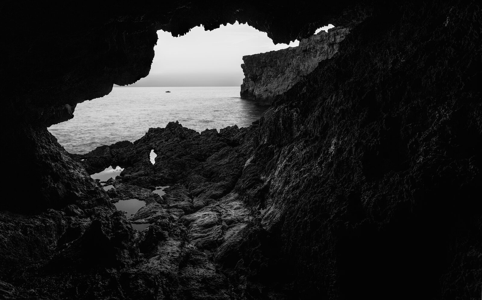 A lone figure in the mouth of a sea cave at Għar Lapsi, black and white