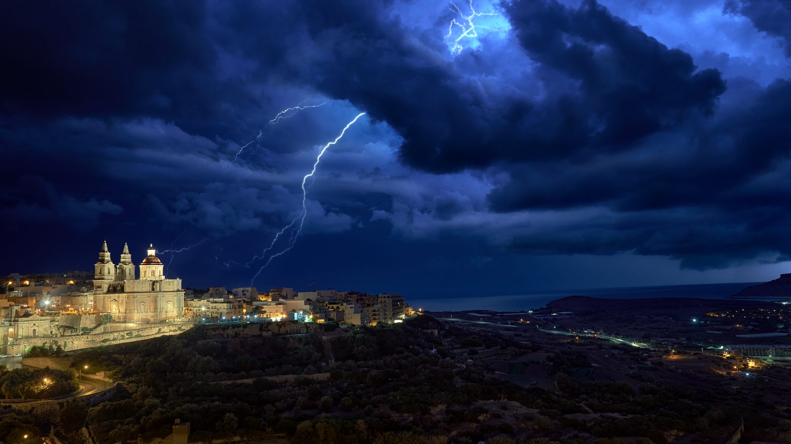 A lightning bolt striking above the lit town of Mellieħa at night