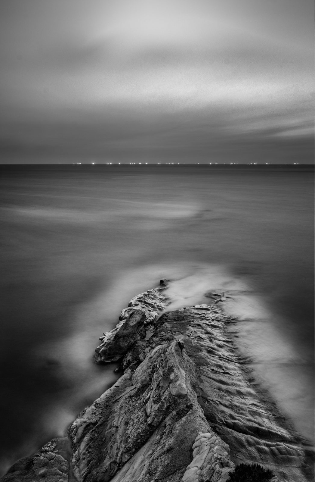 A rock spur running into a smooth sea before sunrise at Munxar, Marsaskala, black and white long exposure