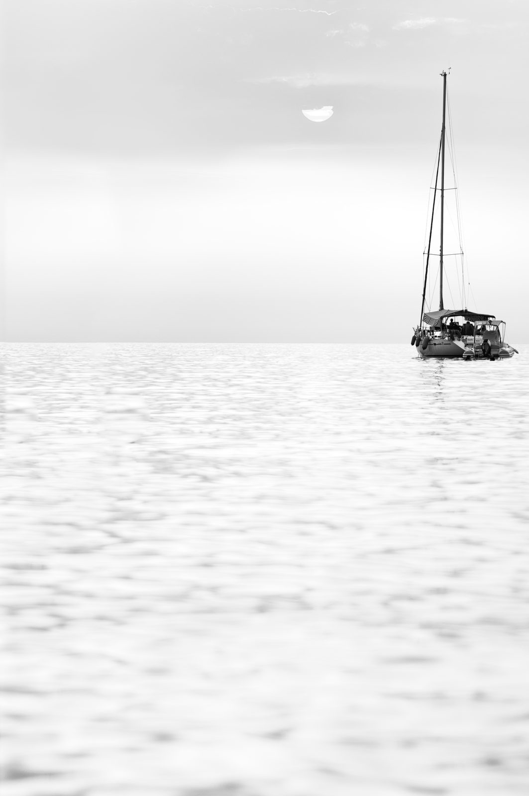 A dark rock rising from a smooth, pale sea in a high-key black and white long exposure
