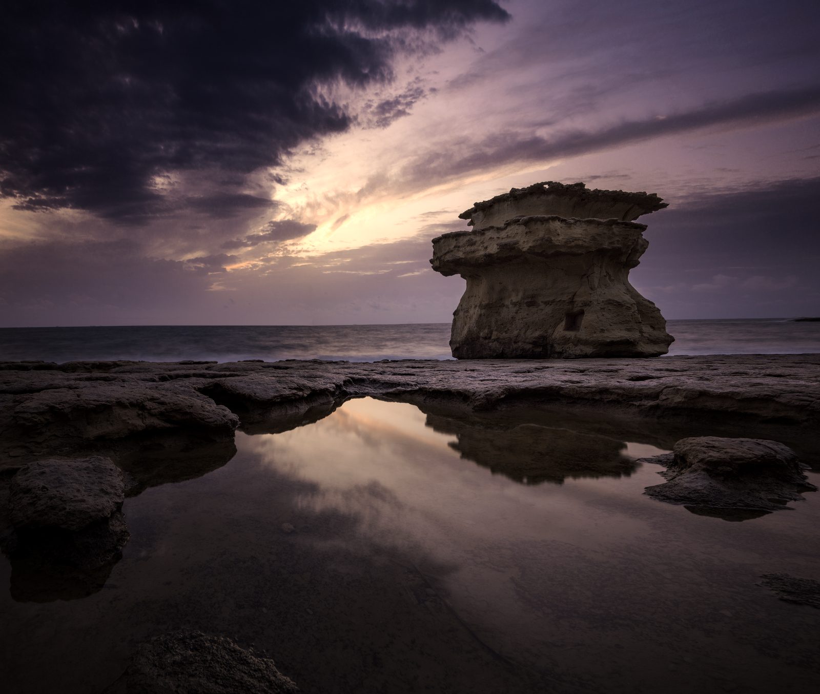 Mushroom rock reflected in a still pool before sunrise at St Peter's Pool, Malta