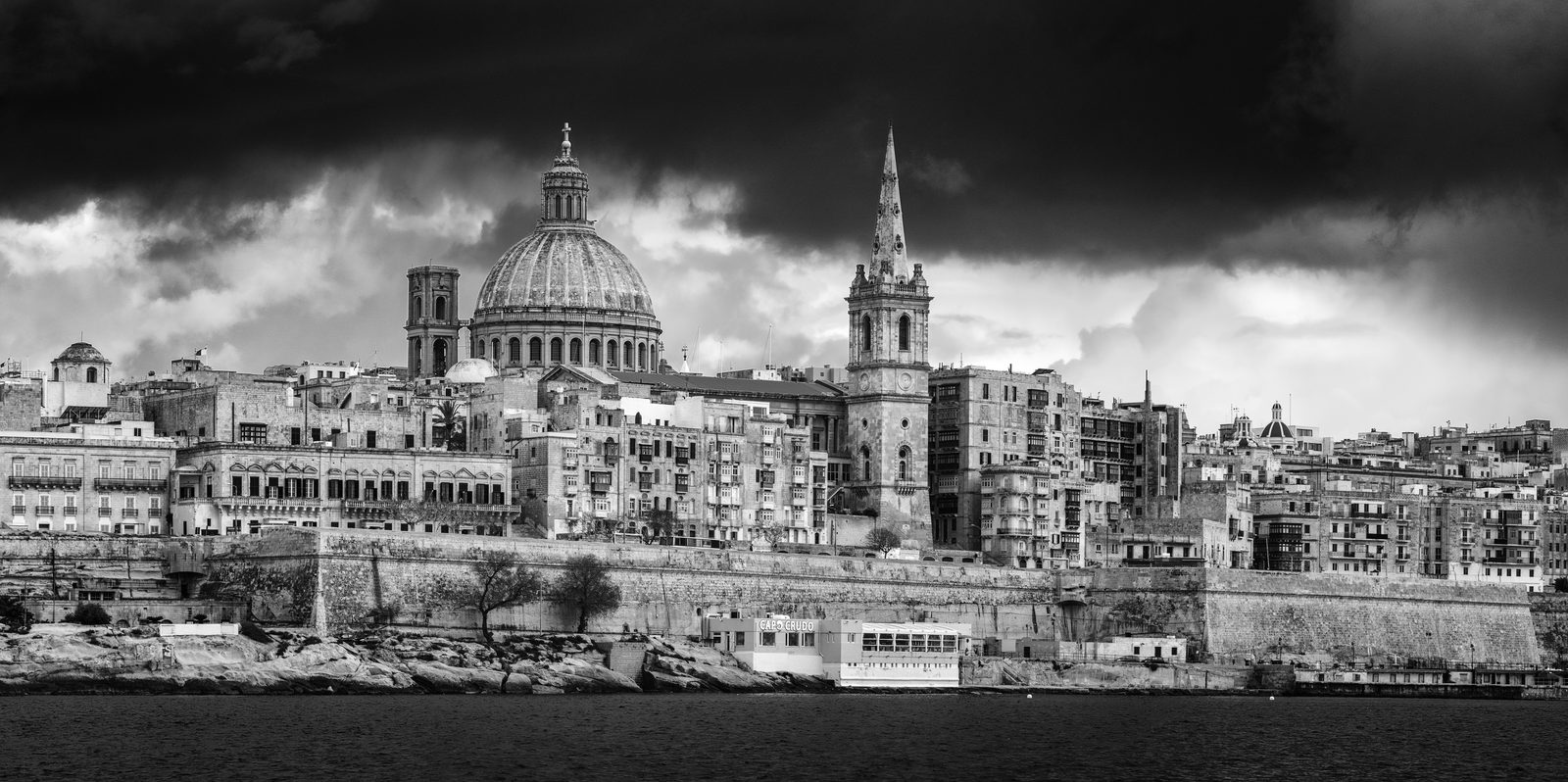 A wide black and white panorama of Valletta under a heavy sky