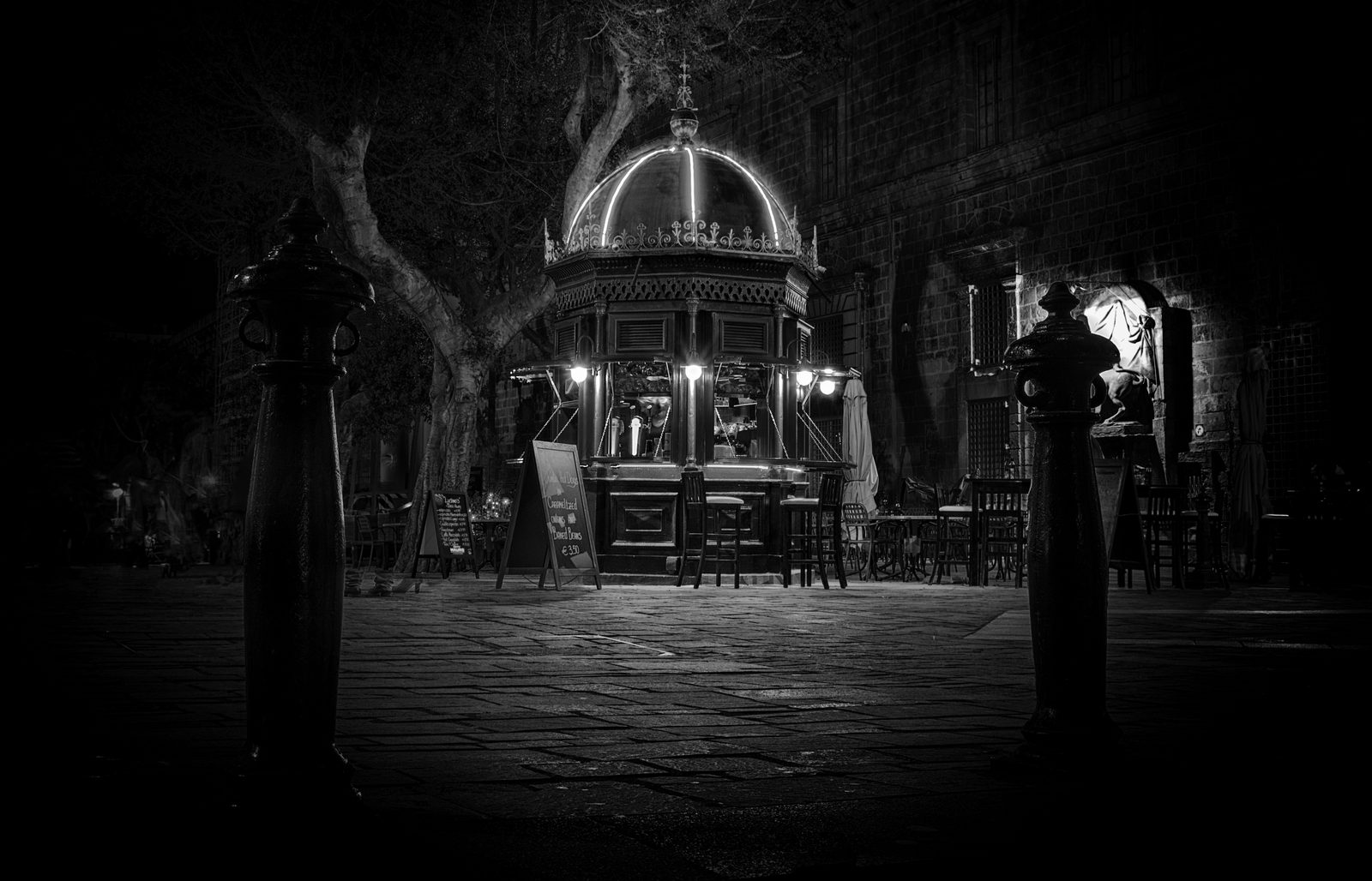 A traditional kiosk glowing at night on Merchants Street, Valletta, black and white