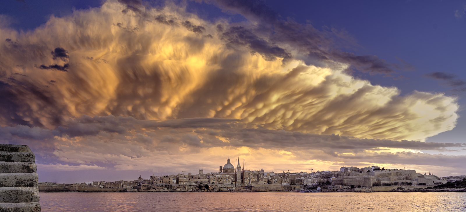 Golden mammatus clouds hanging over the Valletta skyline at sunset, seen from Sliema
