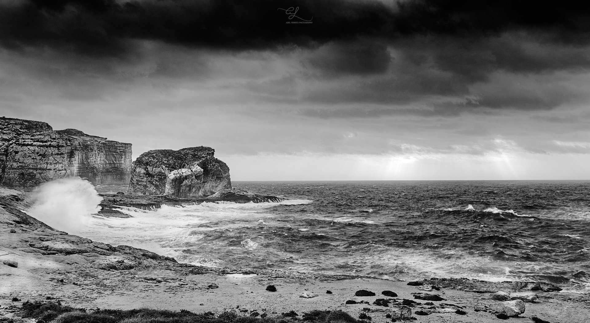 A wave bursting against Ġebla tal-Ġeneral rock in black and white, Dwejra, Gozo